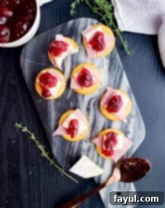 Overhead shot of Cranberry Brie and Ham Ritz Bites arranged on a blue marble serving tray, with fresh thyme and a bowl of cranberry sauce nearby.