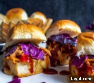 Close-up shot of a single Crockpot Hawaiian BBQ Chicken Slider, with two other sliders blurred in the background, on a white plate.