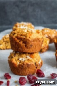 This Morning Glory Muffins Recipe is the best easy, healthy, and quick breakfast of brunch! Filled with carrots, cranberries, apples, applesauce and nuts you will love this clean eating favorite perfect for kids and adults! #Vegan #CleanEating #Healthy #Food #recipe Two Morning glory muffins stacked on top of each other on white parchment paper.