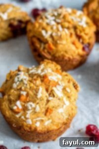 This Morning Glory Muffins Recipe is the best easy, healthy, and quick breakfast of brunch! Filled with carrots, cranberries, apples, applesauce and nuts you will love this clean eating favorite perfect for kids and adults! #Vegan #CleanEating #Healthy #Food #recipe The image shows the muffins on parchment paper. The image is shot from 45 degrees and shows two muffins focused on the tops with some blurred out in the background.