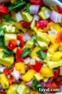 Close up of freshly chopped ingredients for mango avocado salsa in a mixing bowl, ready to be combined.