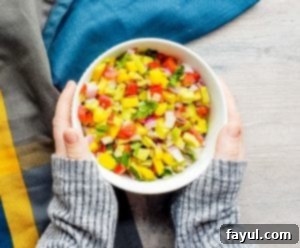 A close-up shot of creamy, colorful mango avocado salsa in a white bowl, being held by two hands, ready to be enjoyed.