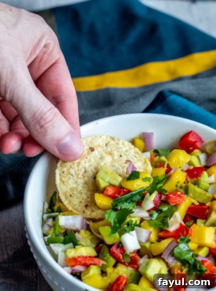 A hand dipping a crispy tortilla chip into a bowl of fresh, vibrant mango avocado salsa, highlighting its dip-ability.