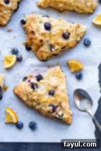 These Blueberry White Chocolate Scones with Lemon Glaze are the perfect sweet breakfast or afternoon tea treat! This easy dessert recipe will be your new family favorite! #scones #breakfast #dessert #blueberry #recipe Blueberry white chocolate scones on a piece of parchment with blues lemon slices.