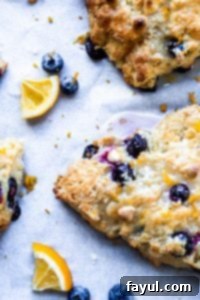 These Blueberry White Chocolate Scones with Lemon Glaze are the perfect sweet breakfast or afternoon tea treat! This easy dessert recipe will be your new family favorite! #scones #breakfast #dessert #blueberry #recipe Close up overhead of blueberry scone on white parchment paper.