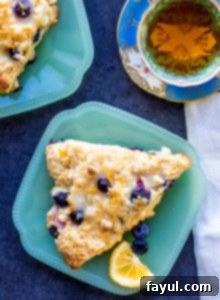 These Blueberry White Chocolate Scones with Lemon Glaze are the perfect sweet breakfast or afternoon tea treat! This easy dessert recipe will be your new family favorite! #scones #breakfast #dessert #blueberry #recipe Overhead shot of two blueberry scones on teal plates with a cup of tea.