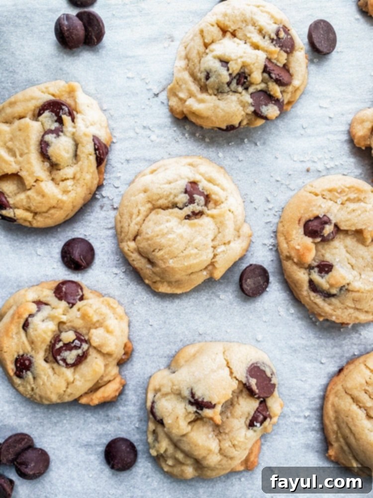 An overhead shot of freshly baked salted chocolate chip cookies laid out on parchment paper, highlighting their golden-brown edges and the subtle gleam of sea salt crystals on top.