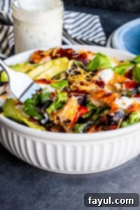Smoky BBQ Chicken Salad with Creamy Buttermilk Ranch 3 A silver fork dipping into a white bowl filled with a colorful BBQ Chicken Salad, showcasing the fresh ingredients and the dressing.
