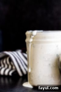 Buttermilk ranch dressing in a glass mason jar spilling over the side on a dark blue counter.