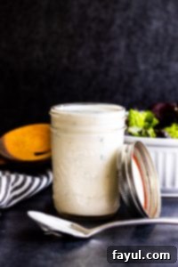 Strait on shot of ranch filled mason jar with silver spoon in front sitting on counter top.
