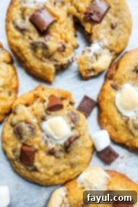 Overhead shot of freshly baked S'mores cookies on white parchment paper, with one cookie cut in half to show the gooey center.
