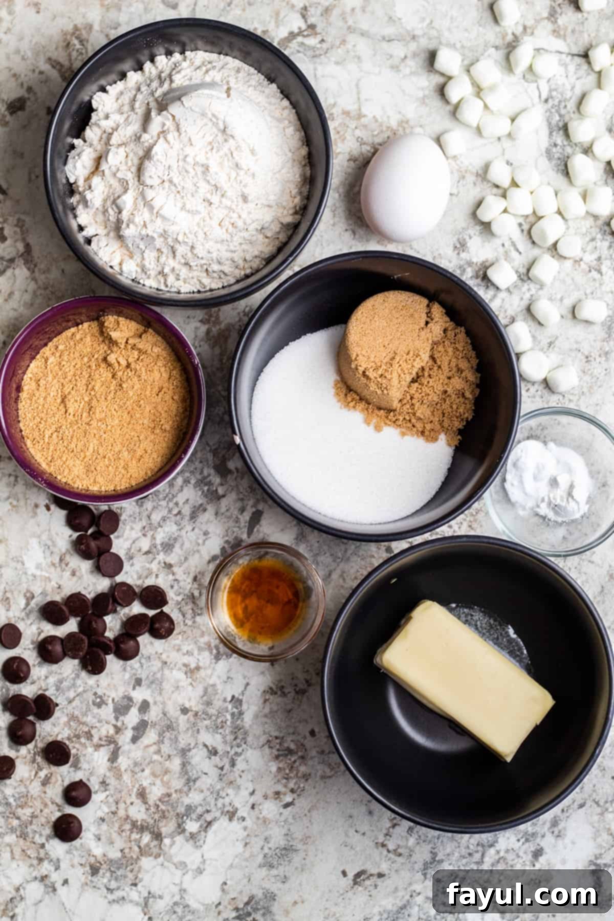 Overhead shot of s'mores cookie ingredients in small bowls on a white counter.