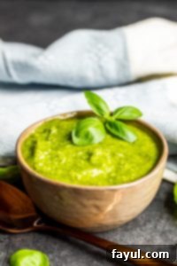 Basil pesto sauce in a gray bowl with a gold spoon next to it.