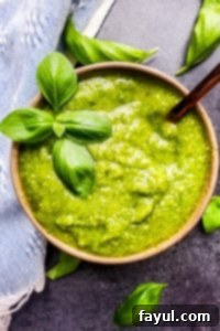 Overhead shot of basil pesto with gold spoon in the bowl and leaves surrounding it.