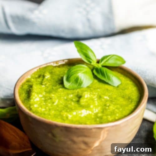 Basil pesto sauce in a gray bowl with a gold spoon next to it.