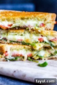 This Grilled Goat Cheese Sandwich recipe is perfect for an easy lunch or weeknight dinner for the family. This fancy grilled cheese is filled with goat cheese, mozzarella, tomatoes, arugula, homemade basil pesto and avocado! This vegetarian sandwich is ready in about 15 minutes and can be customized with meat or additional cheese. Step by step instructions and VIDEO included! #grilledcheese #sandwich #recipe #lunch #pesto #vegetarian #vegetarianfood #meatlessmonday Close up strait on shot of grilled cheese cut in half and piled on top of each other, showcasing melted cheese and fresh greens.