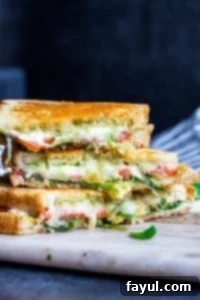 This simple Grilled Goat Cheese Sandwich recipe is perfect for an easy lunch or weeknight dinner for the family. This fancy grilled cheese is filled with goat cheese, mozzarella, tomatoes, arugula, homemade basil pesto and avocado! This vegetarian sandwich is ready in about 15 minutes and can be customized with meat or additional cheese. Step by step instructions, photos, and VIDEO included! #grilledcheese #sandwich #recipe #lunch #pesto #vegetarian Strait on shot of stacked grilled cheese sandwiches with a dark blue background, showcasing the beautiful golden crust.