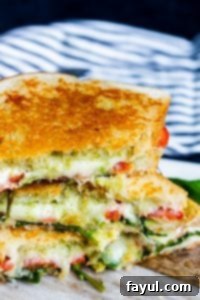 This Grilled Goat Cheese Sandwich recipe is perfect for an easy lunch or weeknight dinner for the family. This fancy grilled cheese is filled with goat cheese, mozzarella, tomatoes, arugula, homemade basil pesto and avocado! This vegetarian sandwich is ready in about 15 minutes and can be customized with meat or additional cheese. Step by step instructions and VIDEO included! #grilledcheese #sandwich #recipe #lunch #pesto #vegetarian #food Angle shot of grilled cheese stacked on top of each other on top of a wood and white marble cutting board, highlighting the layers inside.