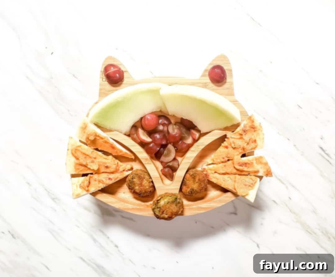 A fox plate for my son's lunch. It features honeydew, grapes, veggie nuggets and hummus on naan bread. The plate is sitting on a marble table. 