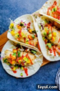 Overhead shot of two healthy fish tacos artfully arranged on a rustic wooden cutting board, set against a vibrant blue countertop.