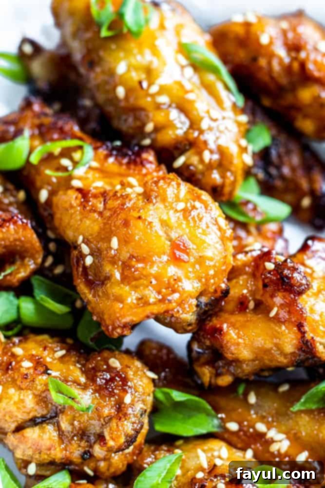Close up shot of several golden brown air fryer sweet chili chicken wings garnished with sesame seeds.