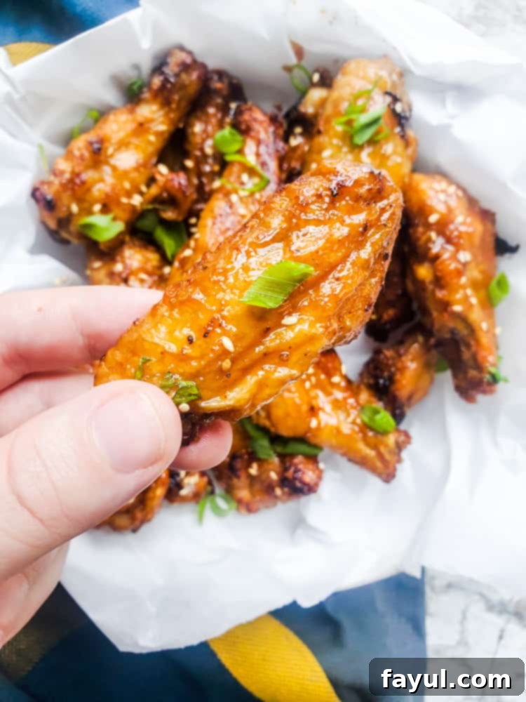 Hand holding a sweet chili chicken wing over a bowl of wings, showcasing the crispy texture and sticky sauce.