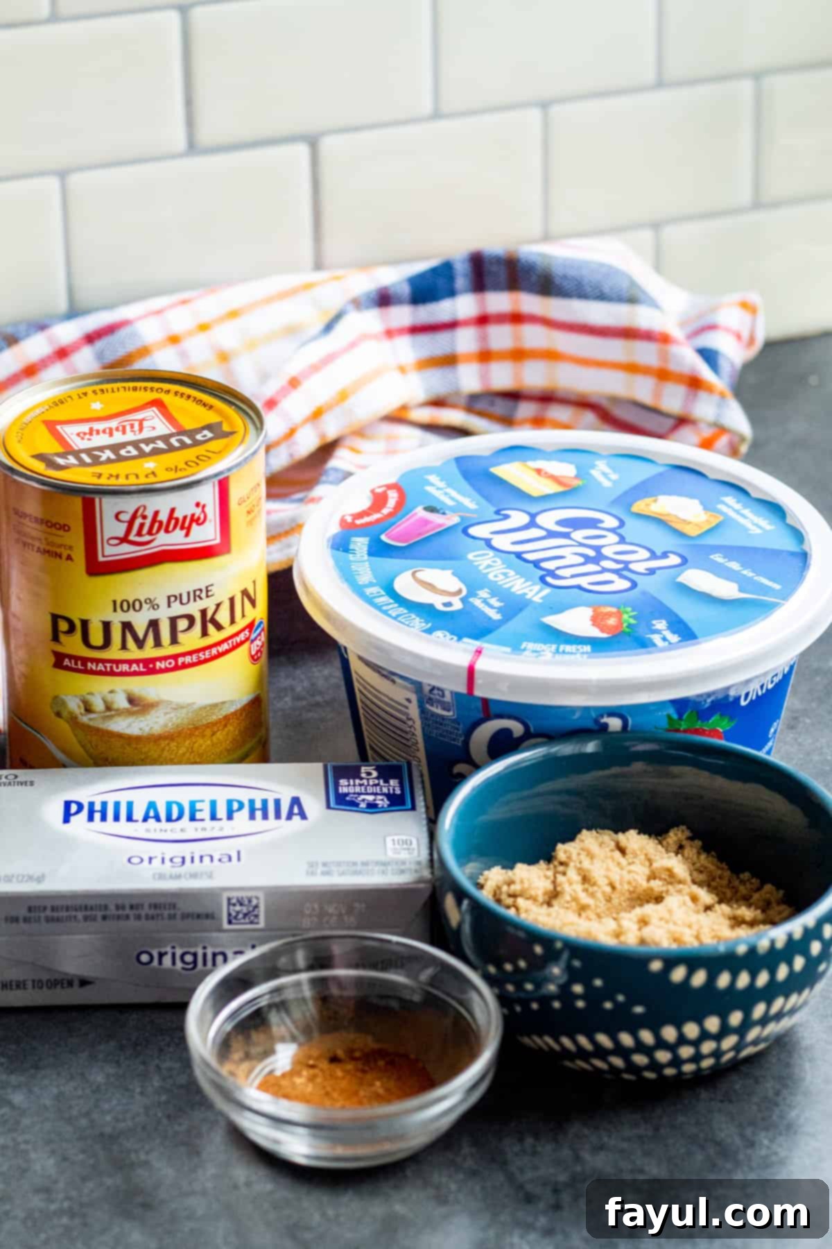 Fresh ingredients for no-bake pumpkin dip laid out on a vibrant blue counter, showcasing canned pumpkin, cream cheese, whipped topping, brown sugar, and pumpkin pie spice.