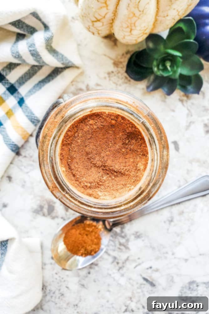 Craft Your Own Pumpkin Pie Spice Blend 2 Overhead shot of pumpkin spice in a glass jar on a white counter with silver spoon next to it.