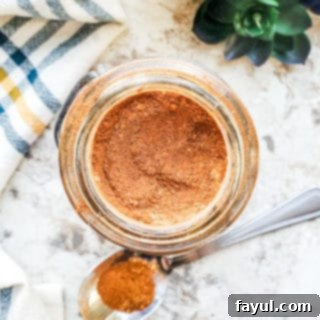 Overhead shot of pumpkin spice in a glass jar on a white counter with silver spoon next to it.