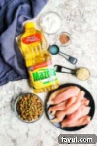 Step-by-step guide to making Pistachio Crusted Baked Chicken Tenders. This easy 30-minute healthy recipe is great for kids and adults, and perfect for meal prepping work lunches. The process involves dunking chicken in Greek yogurt and Mazola Corn Oil, then coating with crushed pistachios for a superior chicken tender alternative. Includes detailed instructions. #chickentenders #healthy #keto #lowcard #paleo A vibrant collection of ingredients laid out on a clean white counter, featuring fresh chicken tenders, a bowl of creamy Greek yogurt, golden Mazola Corn Oil, bright green pistachios, and a medley of colorful spices, hinting at the flavorful meal to come.