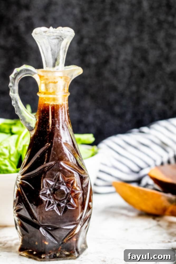 This Homemade Balsamic Vinaigrette Dressing goes great with salads, wraps or as a marinade for meats. This easy and healthy dressing is ready in only 5 minutes and requires no cooking! You will love this light dressing packed with honey, olive oil, balsamic vinegar, garlic and spices. {VIDEO}. #dressing #healthy #vegetarian #glutenfree Glass bottle of balsamic vinaigrette on a white counter with salad in the background.