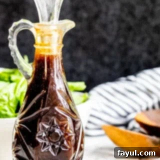 Glass bottle of balsamic vinaigrette on a white counter with salad in the background.
