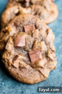Irresistible Chewy Double Chocolate Chip Cookies with Semi-Sweet Chocolate Chunks and Karo Corn Syrup. A quick, no-chill recipe perfect for holiday baking or a delightful treat, ready in about 20 minutes. Close up shot of chewy double chocolate chip cookies in a line on a blue counter, highlighting their rich color and chocolate chunks.
