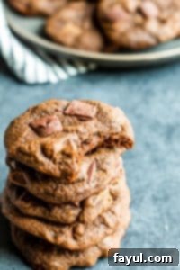 A stack of delicious Chewy Double Chocolate Chip Cookies, featuring a perfect bite taken out of one to show its rich, gooey texture. Made with Karo Corn Syrup. Double chocolate chip cookies stacked on top of each other on a blue counter, with a bite taken out of the top one revealing its soft, chewy interior.