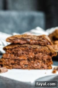 A close-up of Chewy Double Chocolate Chip Cookies, showcasing their rich color and abundant chocolate chunks, perfect for any sweet craving. Straight on shot of perfectly baked double chocolate chip cookies, stacked and one cut in half on parchment paper, showing the soft inside and melted chocolate chunks.