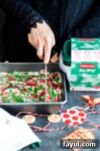Slicing homemade sugar cookie fudge for holiday serving. A hand slicing festive sugar cookie fudge into squares within a parchment-lined baking dish.