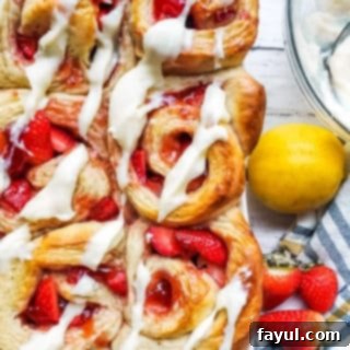 Overhead shot of strawberry rolls in a large baking dish on a white counter with bowl of icing next to it.
