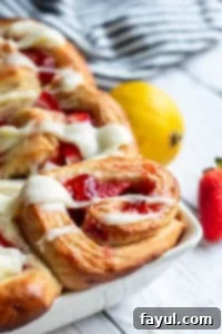 Close up shot of several strawberry cinnamon rolls arranged in a white baking dish on a white counter.