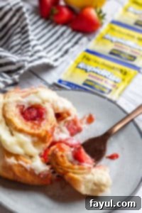 A strawberry roll on a gray plate with a gold fork cutting into it, revealing the layers.