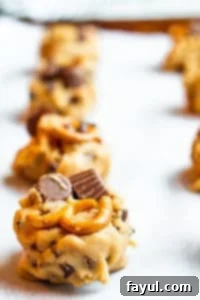 Raw peanut butter cookie dough balls with visible peanut butter cups and pretzels, arranged in rows on a parchment-lined baking sheet.