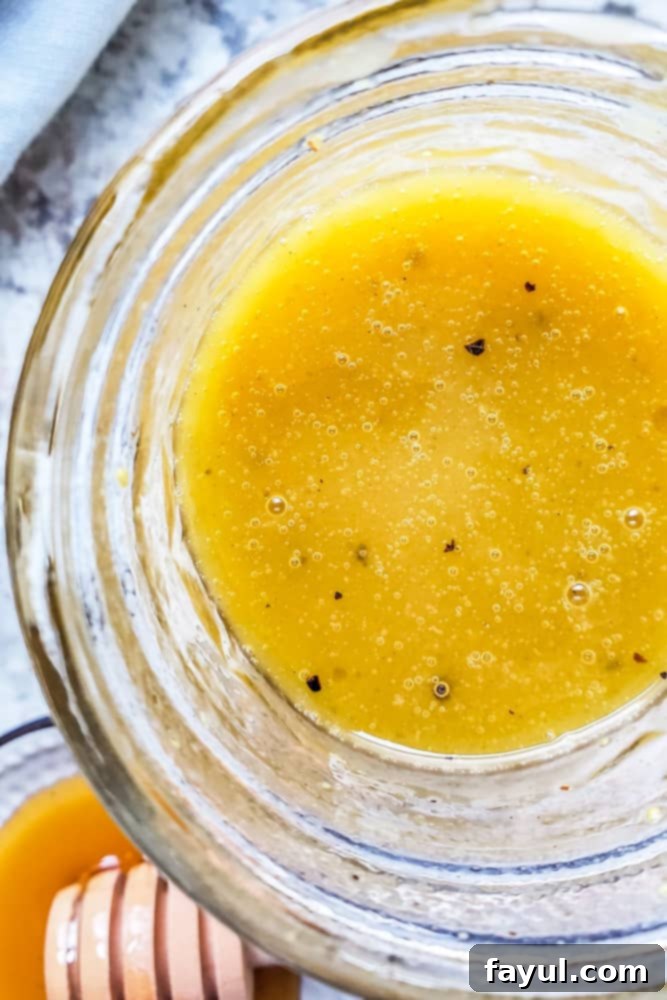 This Homemade Honey Dijon Vinaigrette Dressing recipe is super easy, ready in only 5 minutes and requires no cooking. This honey mustard dressing is great with salads, wraps, veggies, or as a marinade. This salad dressing is vegetarian, gluten-free, healthy and perfect for both kids and adults. Step by step photos and recipe ideas and suggestions included! #dressing #vegetarian #healthy Overhead close up shot of honey mustard dressing in a glass mason jar on a white counter.