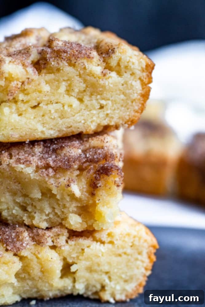 A stack of golden brown Snickerdoodle Blondies dusted with cinnamon sugar, set on a vibrant blue countertop.