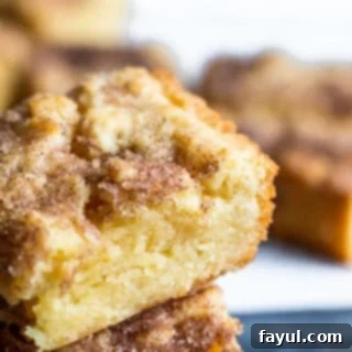 A close-up shot of a stack of golden brown snickerdoodle blondies on a white counter, with more blondies blurred in the background.
