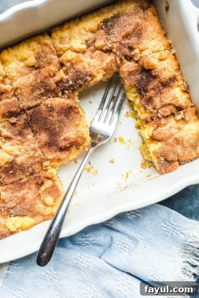 Freshly baked Snickerdoodle Blondies in a white baking dish, with a few slices already cut and a silver fork resting on the top of a blondie.