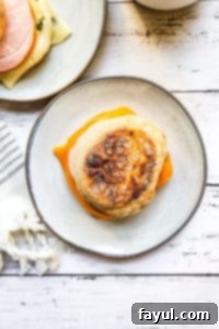 Make Ahead Breakfast Sandwiches: Easy, quick, and freezer-friendly with eggs, veggies, Canadian bacon, and cheese on an English muffin. Perfect for meal prep! Another view of a make-ahead breakfast sandwich on a gray plate, with a second blurred sandwich in the background, showcasing its delicious layers.