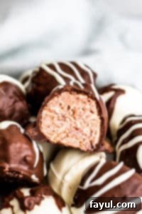 Easy Homemade Raspberry Cheesecake Truffles for Valentine's Day and Special Occasions - Make Ahead & Freezer Friendly! Close-up shot of a raspberry truffle cut in half, revealing its creamy pink interior and fresh raspberry pieces, on a pristine white surface.