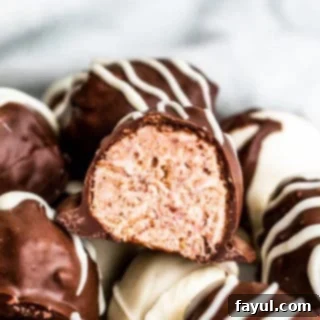 Decadent White Chocolate Raspberry Truffles 3 Straight on shot of raspberry truffle cut in half on a pile of several, showcasing its vibrant raspberry filling.