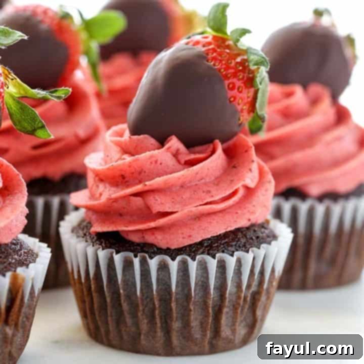 Moist chocolate covered strawberry cupcakes, elegantly topped with strawberry buttercream frosting and a fresh chocolate-dipped strawberry, ideal for Valentine's Day.