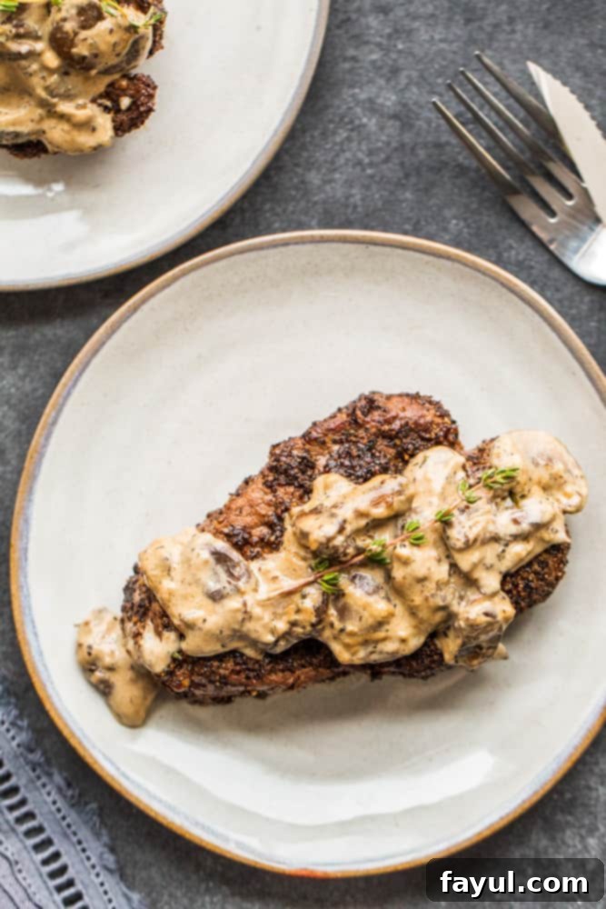 Overhead shot of two steak on gray plates with mushroom sauce on top.