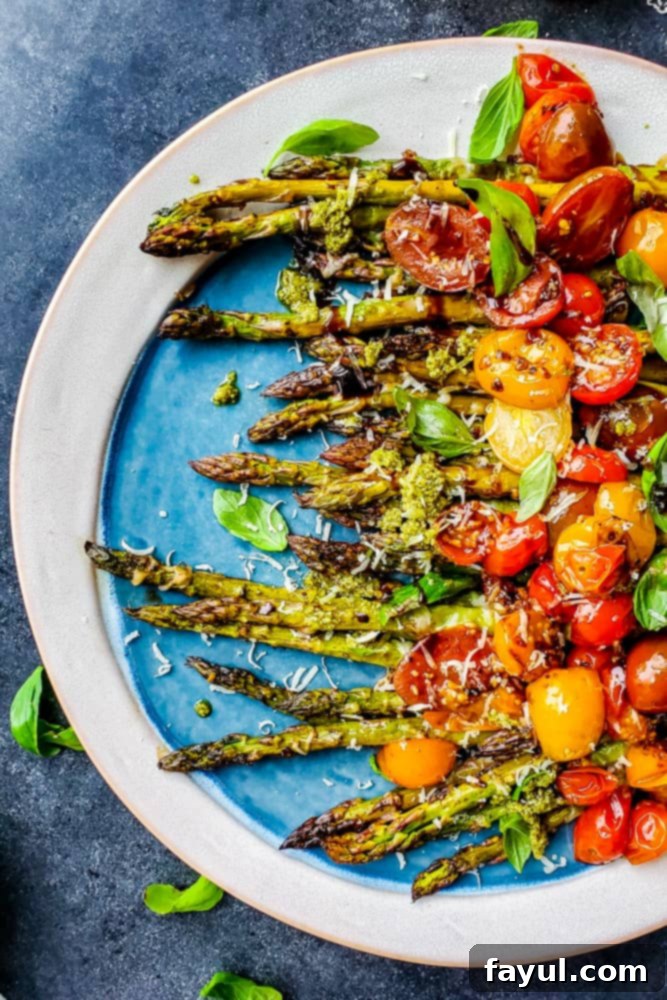 This Balsamic Oven Roasted Asparagus recipe is the perfect side dish! This easy vegetarian recipe is topped with fresh tomatoes, basil, Parmesan cheese, and homemade basil pesto. This side pairs great with chicken, steak, or soup and salad for a healthy pairing. #recipe #vegetarian #healthy Over head shot of asparagus with tomatoes on a blue and white serving dish, ready for dining.